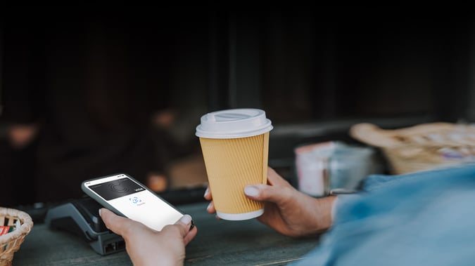 En person som håller i en take-away-kaffe och betalar med sin digitala plånbok och CarPaykortet
